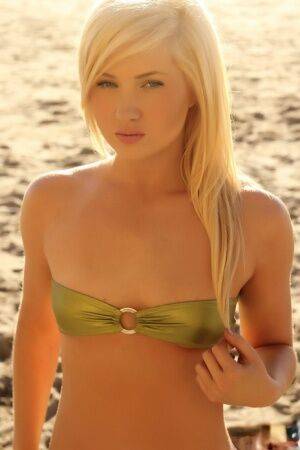 Young looking blonde girl Ashlie Madison cups her flat chest via bikini top on nudepicso.com