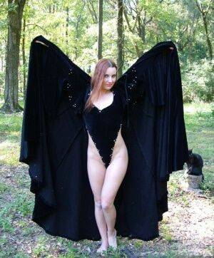 Redhead amateur Amber Lily models nude in a forest draped in a black cape on nudepicso.com