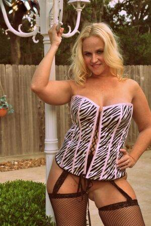 Blonde amateur Dee Siren models a laced corset and mesh hosiery in a backyard on nudepicso.com