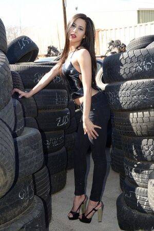 Latina amateur Bella Quinn covers her naked tits with hands amid tire stacks on nudepicso.com