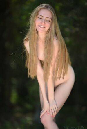 Caucasian teen Lena Flora removes a sexy dress for nude poses on a stump on nudepicso.com