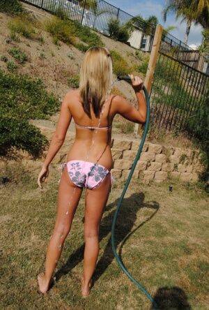 Young blonde girl in a bikini soaks herself with a garden hose on nudepicso.com