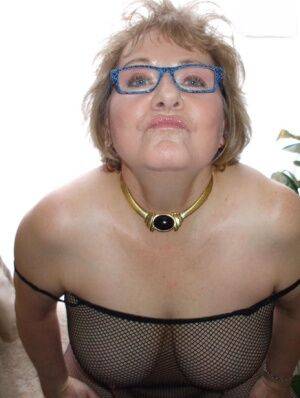 Mature woman Busty Bliss models a mesh bodystocking and glasses on nudepicso.com