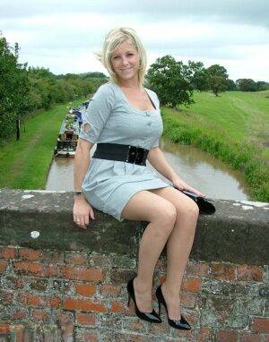 Blonde female sits atop a bridge in a dress and nylons with shiny pumps on nudepicso.com